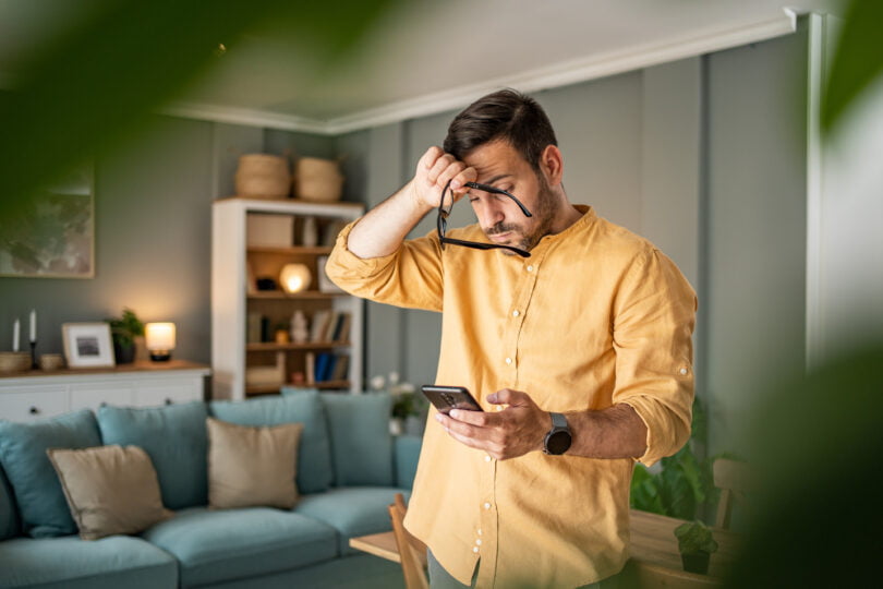 A young man is feeling depressed and thinking about the bad news he is reading online through his smartphone
