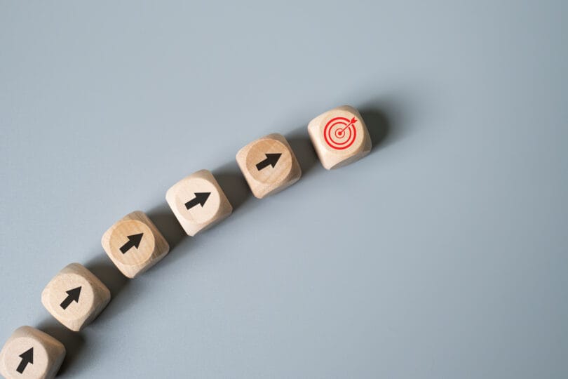Pointing arrow with the improving direction to dart board on wood cube describe for business plan and strategy to achieve target or goal with copy space for text.