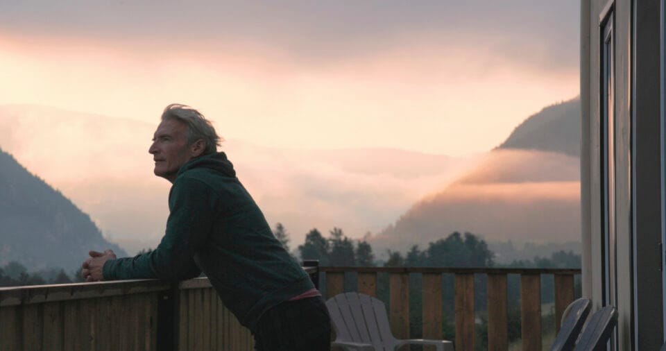 Crop of mature man watches sunrise over mountains from cabin veranda in morning, Canadian Rockies