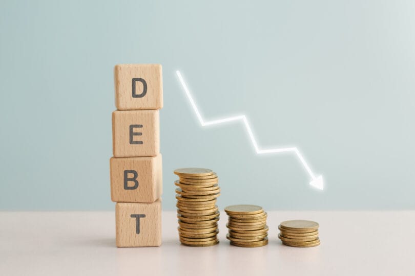 DEBT text on wooden background and stack of coins, down arrow for finance crisis, refinance, earnings management concept