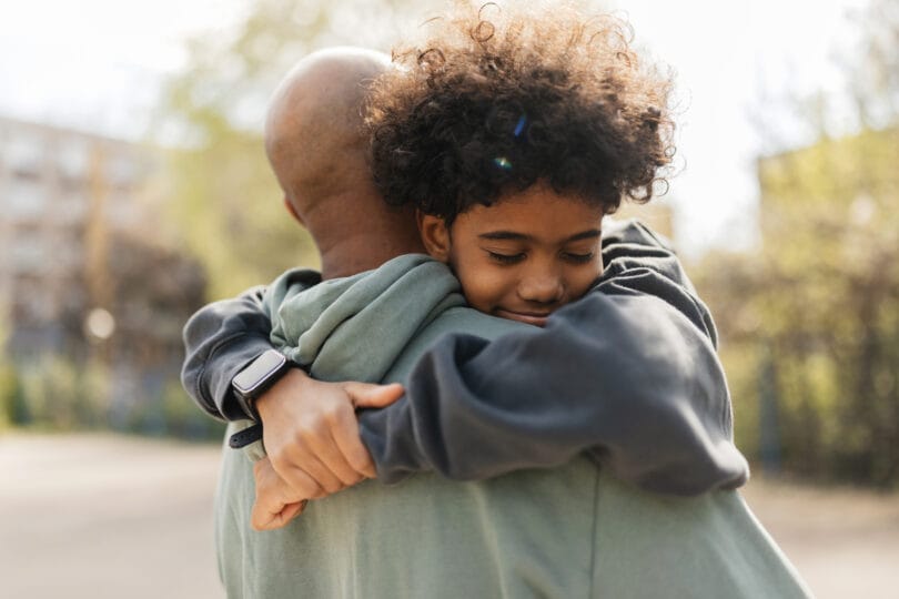 In a touching moment, a child is shown lovingly held in the arms of an adult, emphasizing the emotional connection and protection found within familial relationships.